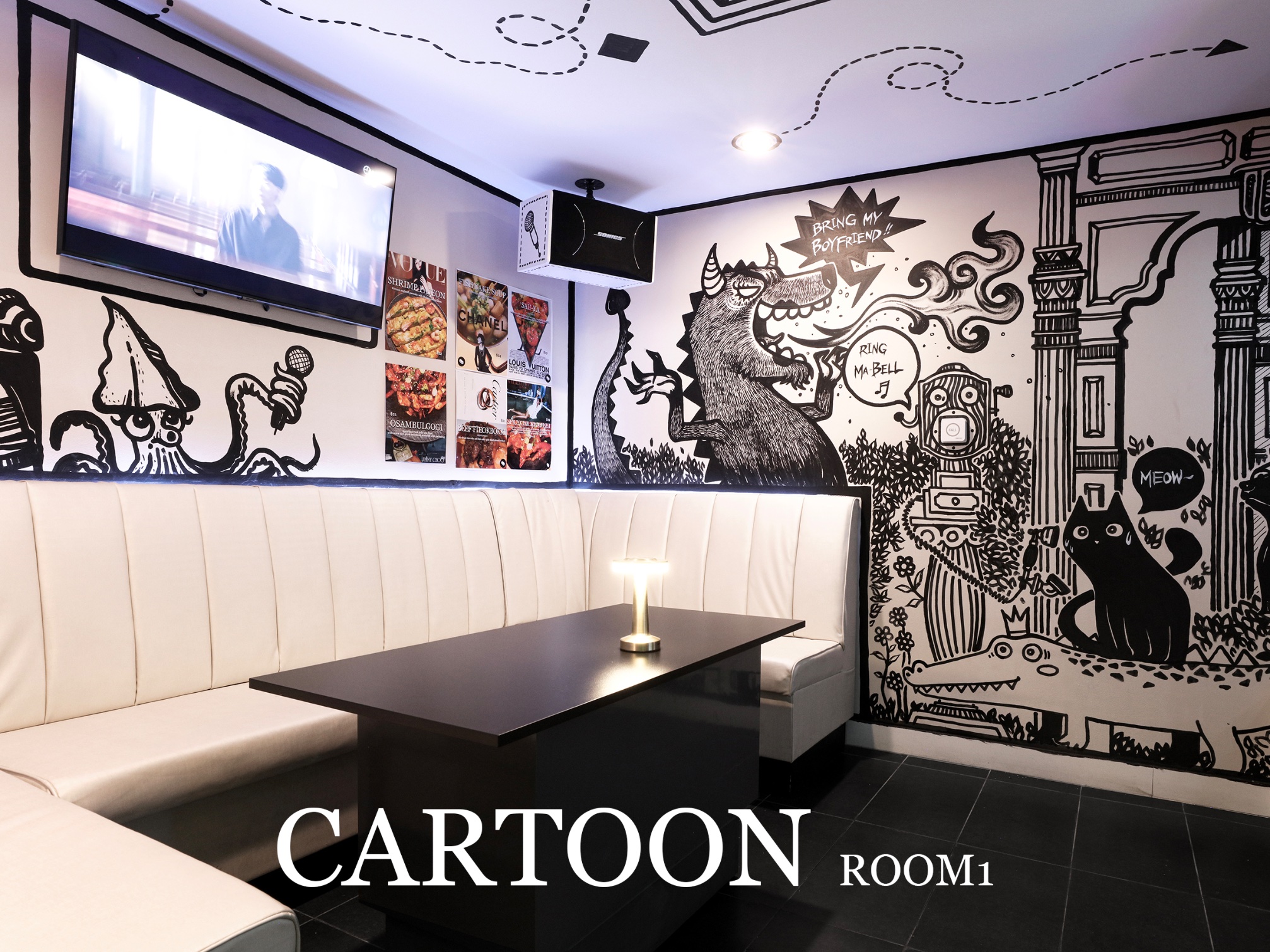 Cartoon-themed private karaoke room with illustrated wall art and white wraparound seating