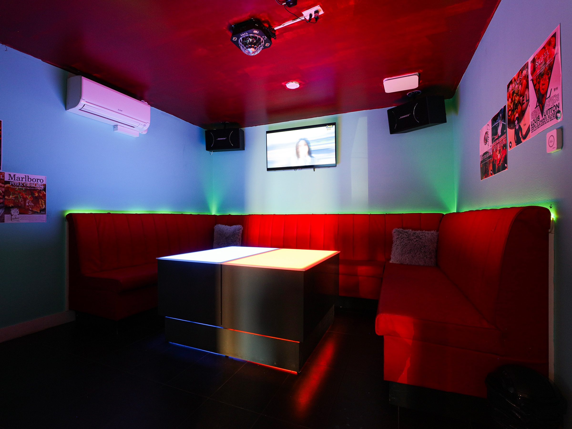 Private karaoke lounge with red seating and colorful neon wall lighting